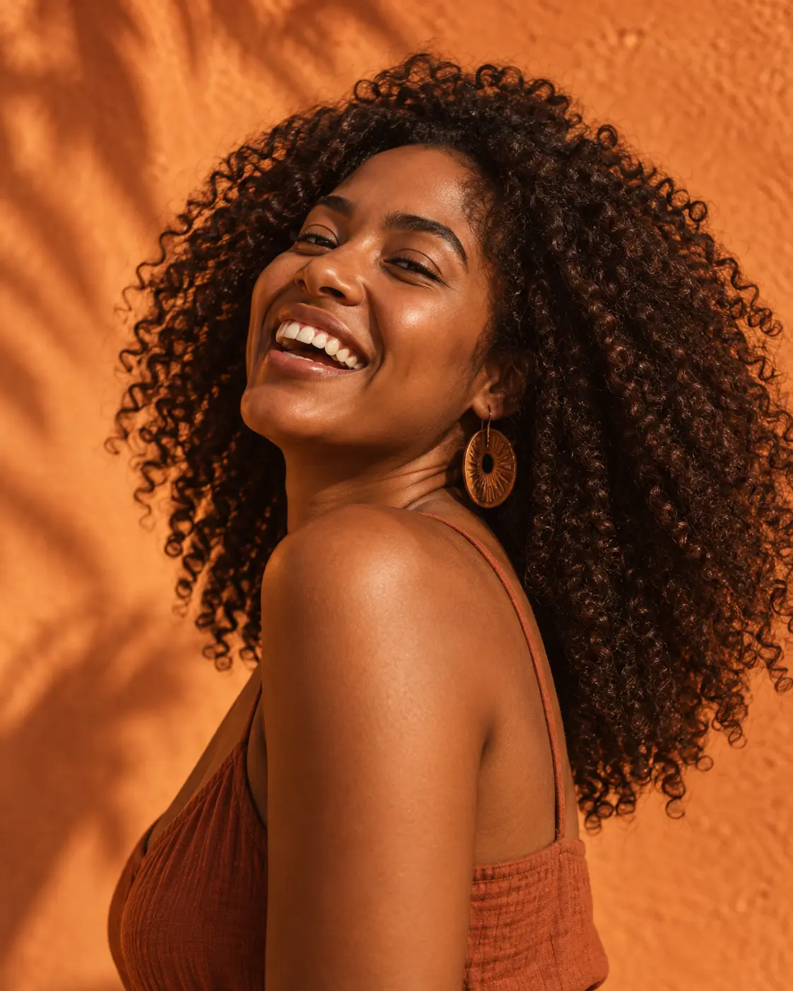 Criadora de cabelo cacheado rindo diante de uma parede terracota